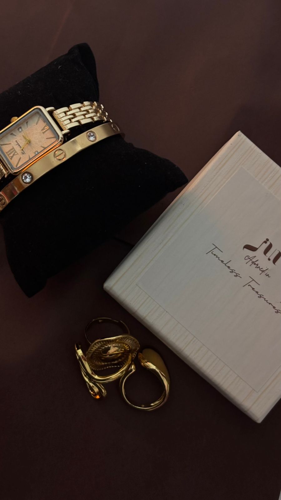 Gold watch, cuff, and rings arranged beside a Juri Jewelry box
